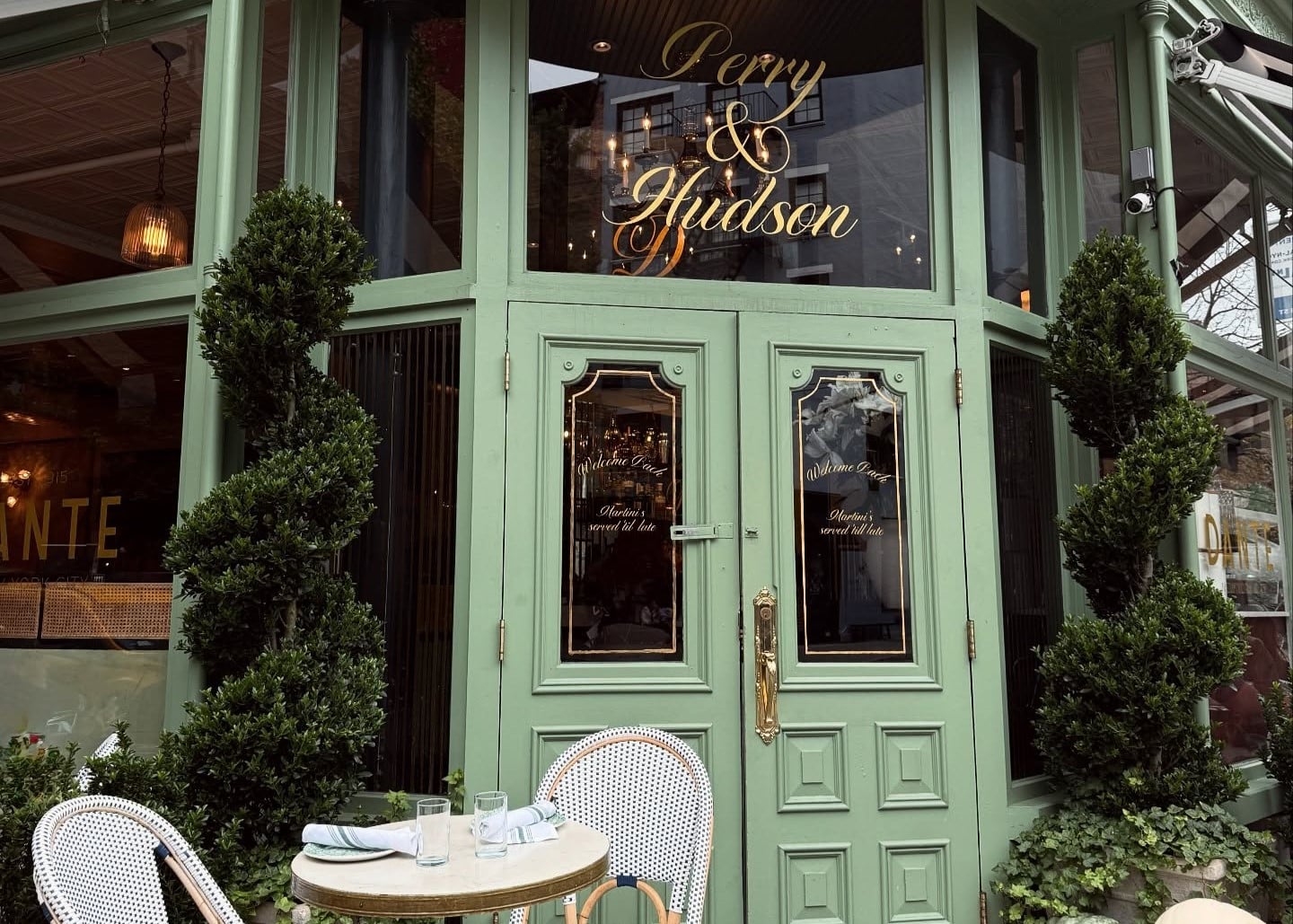 Fachada de um restaurante em Nova York com porta verde e janelas, e uma mesa com duas cadeiras do lado de fora