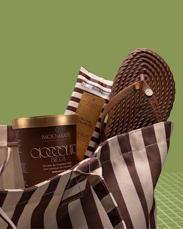 Uma bolsa listrada em marrom e bege traz itens da Bacio di Latte e uma sandália em tom de chocolate, compondo uma cena com estética monocromática.