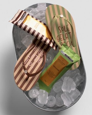 Sandálias listradas e picolés da Bacio di Latte aparecem dispostos sobre gelo, criando uma cena refrescante e colorida.