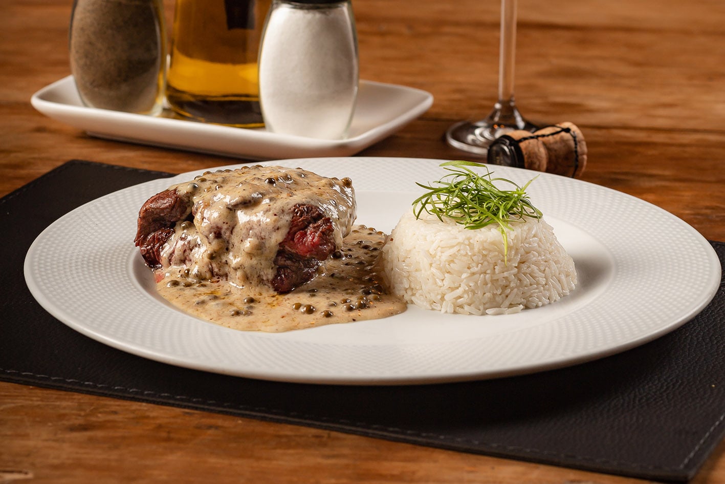 Um filé mignon alto coberto por molho cremoso de pimentas verdes é servido ao lado de um delicado monte de arroz branco com ervas, em uma apresentação sofisticada e apetitosa.